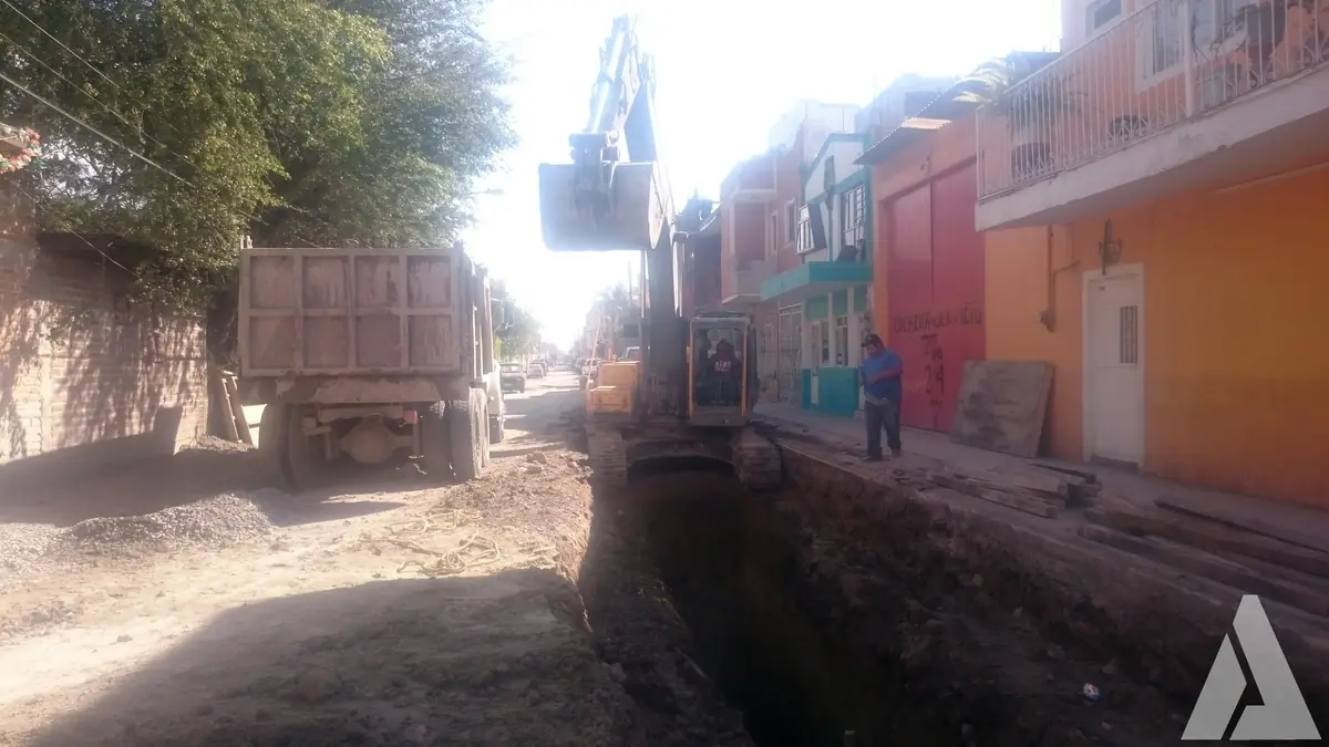 Brazo de excavadora trabajando dentro de la zanja del colector de drenaje en una calle habitada