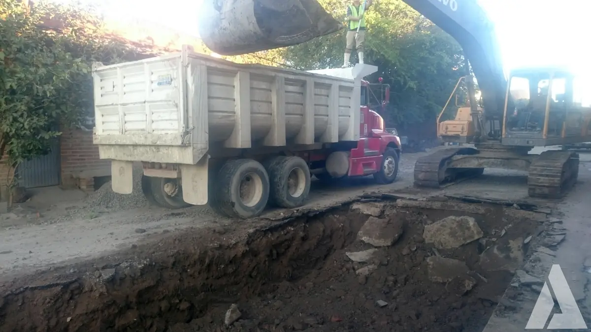 Excavadora cargando un camión de volteo durante la apertura de una zanja de drenaje en una calle urbana