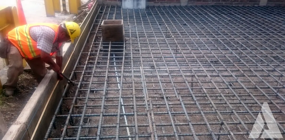 Trabajador con chaleco amarillo amarrando la parrilla de varilla de refuerzo de una losa antes del colado