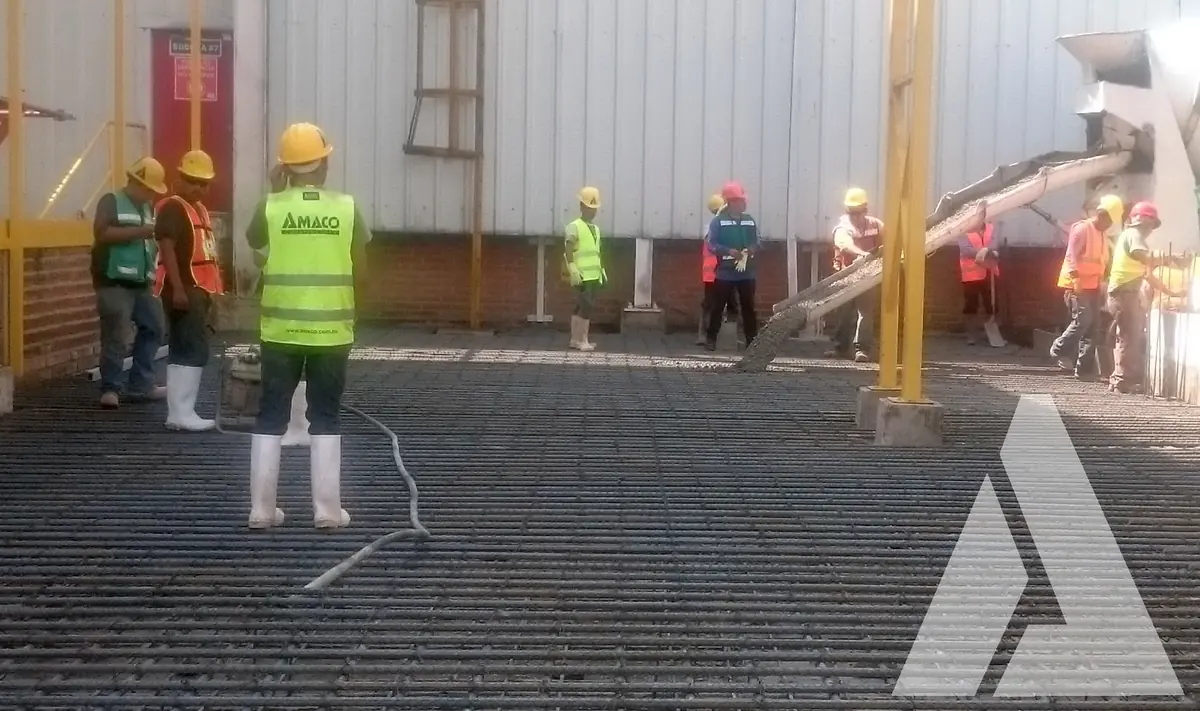 Cuadrilla con cascos y chalecos sobre la parrilla de acero de refuerzo de una losa durante el inicio del colado