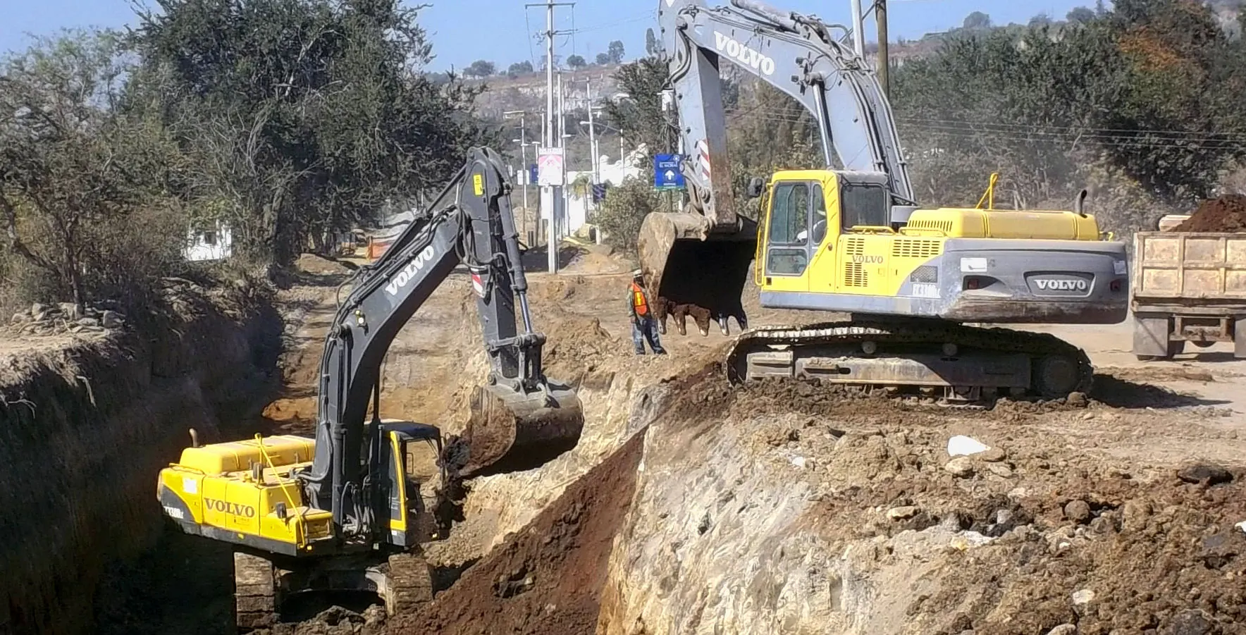 Dos excavadoras Volvo trabajando en la excavación de una zanja profunda para colector de drenaje junto a una carretera